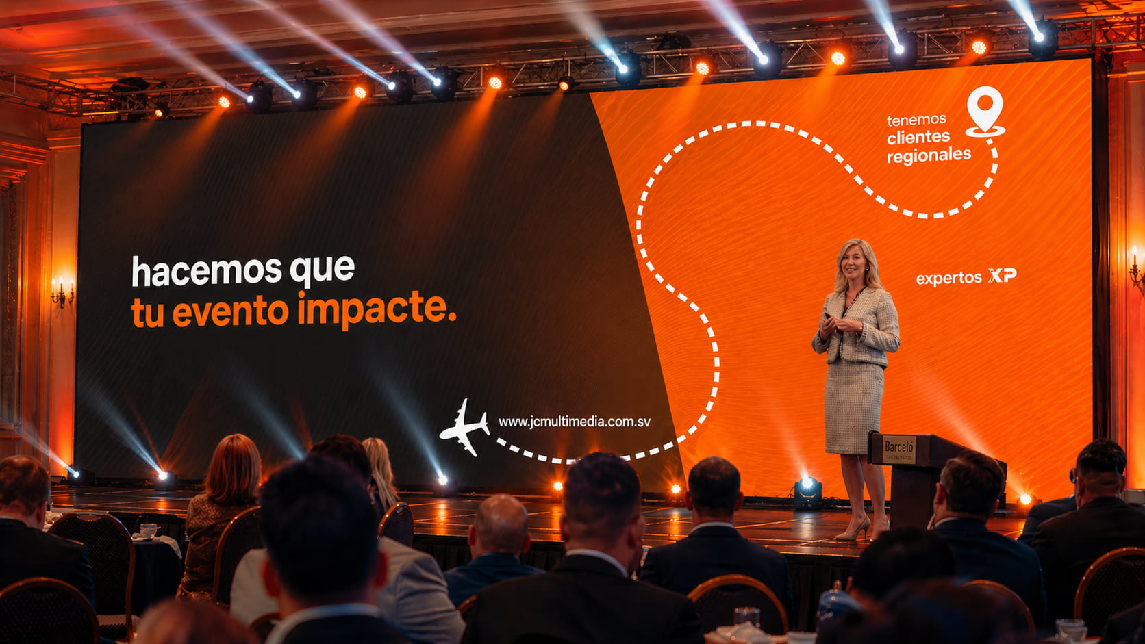Pantalla LED gigante en evento corporativo con iluminación profesional tipo beam en color naranja y blanco, presentación en escenario con branding de JC Multimedia en El Salvador