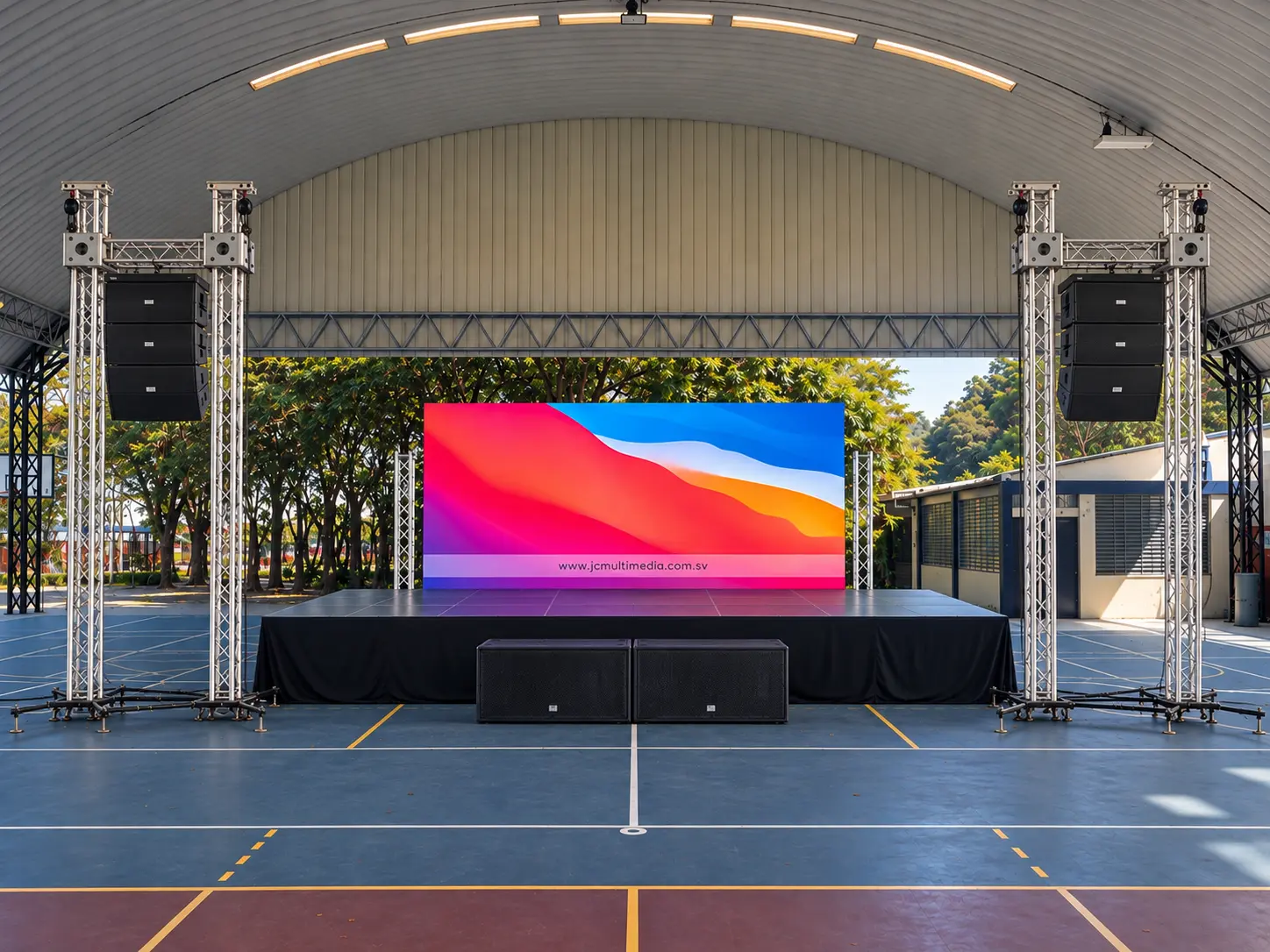 Escenario profesional con line array, subwoofers y pantalla LED sobre estructura de truss en una cancha techada de El Salvador